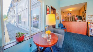 A hotel room with a large window, a small table with a lamp and flowers, a striped sofa, and a reception desk with magazines. - Unicorn Inn by OYO Portland (Portland)