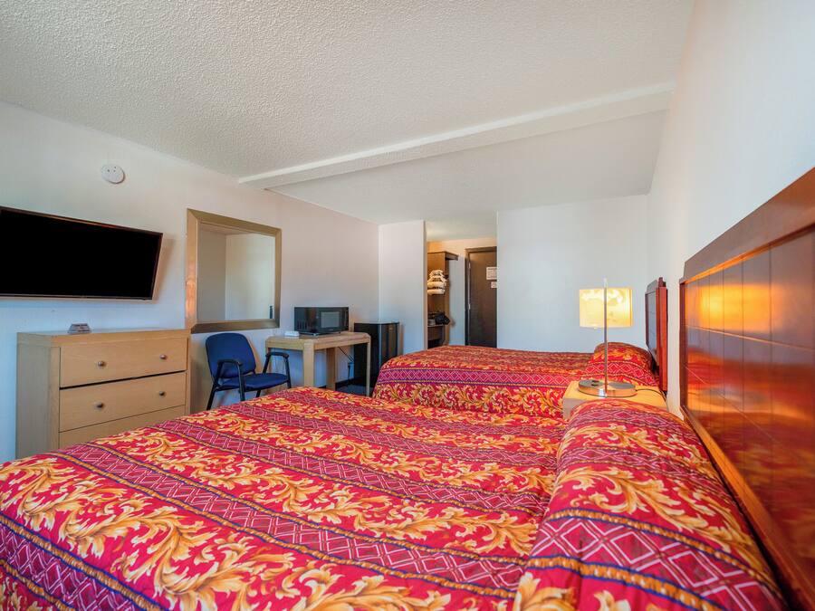 A hotel room with two beds, a desk, a chair, a television, and a mirror.