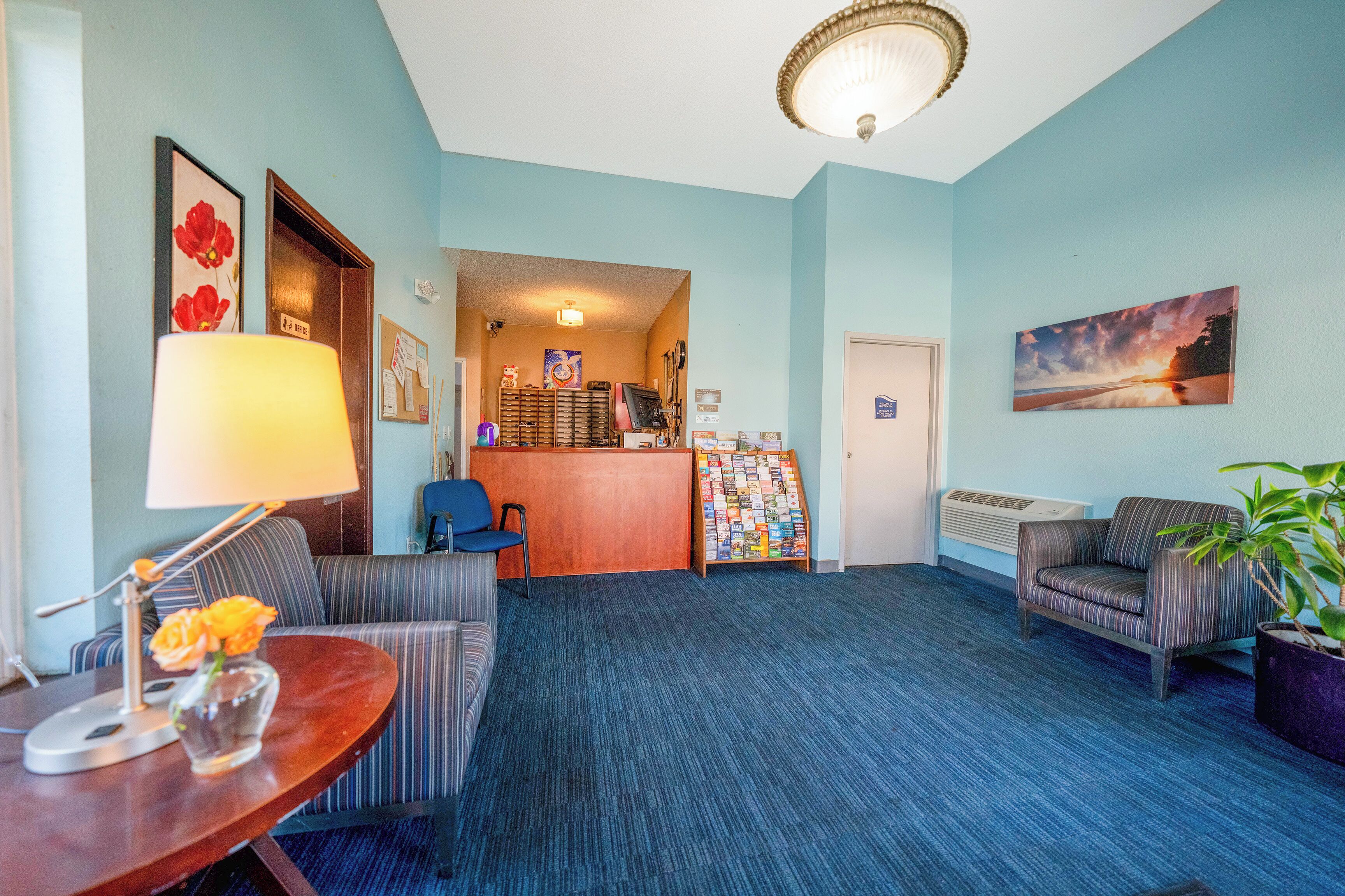Een hotel lobby met gestreepte banken, een receptiebalie, een koffieapparaat en een schilderij aan de muur.