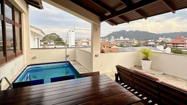 Una terraza en la azotea con piscina, muebles de madera y vistas a la ciudad.