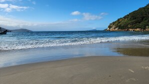 Una playa con olas tranquilas, barcos y un paisaje montañoso al fondo.