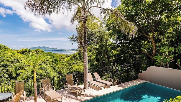 A poolside area with lounge chairs and a view of a natural landscape. - Ocean View 2Br/2Bth Condo In Tamarindo (Tamarindo)