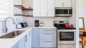 A modern kitchen with white cabinets, stainless steel appliances, a sink, and a countertop with a toaster and coffee maker. - Ocean View 2Br/2Bth Condo In Tamarindo (Tamarindo)