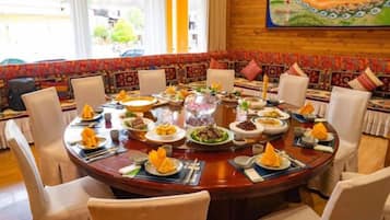 Mesa redonda con varios platos de comida, rodeada de sillas.