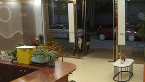 A reception area with a wooden reception desk, potted plants, and a glass door leading outside. - Dinghu Tiantian Business Hotel (Zhaoqing)