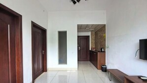 A hallway with wooden doors, a glass partition, a tiled floor, a bench, a trash bin, and a television mounted on the wall. - Dinghu Tiantian Business Hotel (Zhaoqing)