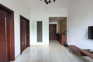 Un pasillo con puertas de madera, un separador de vidrio, suelo de baldosas, un banco, un bote de basura y un televisor montado en la pared.