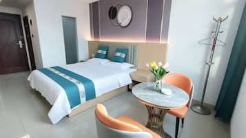 Habitación de hotel con cama, una mesa redonda con sillas, perchero y un reloj de pared.