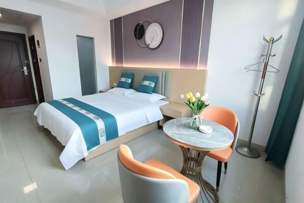 Habitación de hotel con cama, una mesa redonda con sillas, perchero y un reloj de pared.