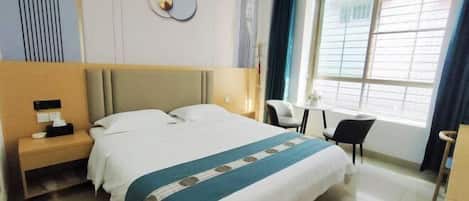 A hotel room with a bed, bedside table, chair, and a window with curtains.