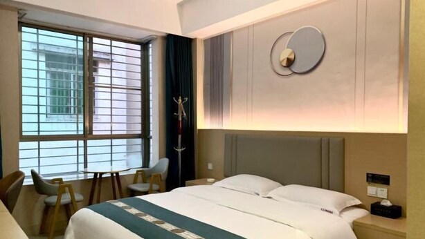 A hotel room with a bed, a desk, a chair, a window, and a wall-mounted clock. - Dinghu Tiantian Business Hotel (Zhaoqing)