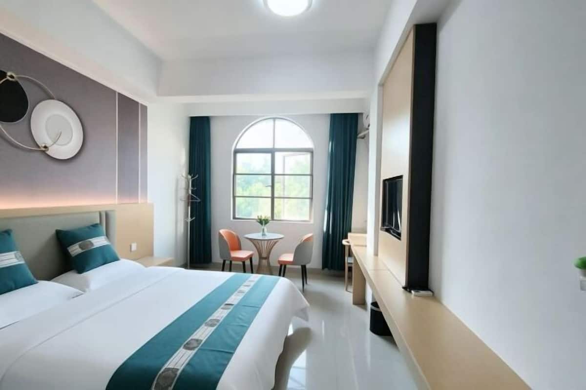 Una habitación de hotel con una cama grande, un escritorio, una silla, una mesita y un televisor.