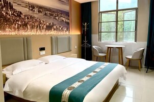 Habitación de hotel con una cama grande, un mural de paisaje urbano, una mesita pequeña, dos sillas y una ventana con vistas a zonas verdes.