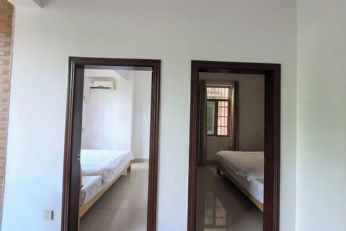 Un estrecho pasillo con dos camas, un muro de ladrillo a la izquierda y una ventana a la derecha.