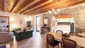 A rustic interior with exposed wooden beams, a stone wall, a dining area with a table and chairs, and a cozy seating area with a sofa and armchairs. - Casa Fornico 2, with terrace and partial lake view in quiet position (Lombardia)