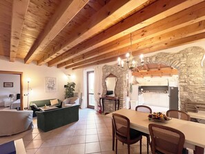A rustic interior with exposed wooden beams, a stone wall, a dining area with a table and chairs, and a cozy seating area with a sofa and armchairs. - Casa Fornico 2, with terrace and partial lake view in quiet position (Lombardia)