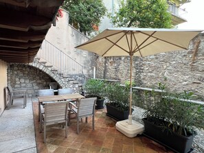 An outdoor patio with a stone wall, wooden furniture, and potted plants. - Casa Fornico 2, with terrace and partial lake view in quiet position (Lombardia)