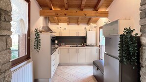 A kitchen with stone walls, wooden beams, and a tiled floor. - Casa Fornico 2, with terrace and partial lake view in quiet position (Lombardia)