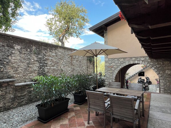 A patio with a stone wall, potted plants, a wooden table, and a scooter. - Casa Fornico 2, with terrace and partial lake view in quiet position (Lombardia)