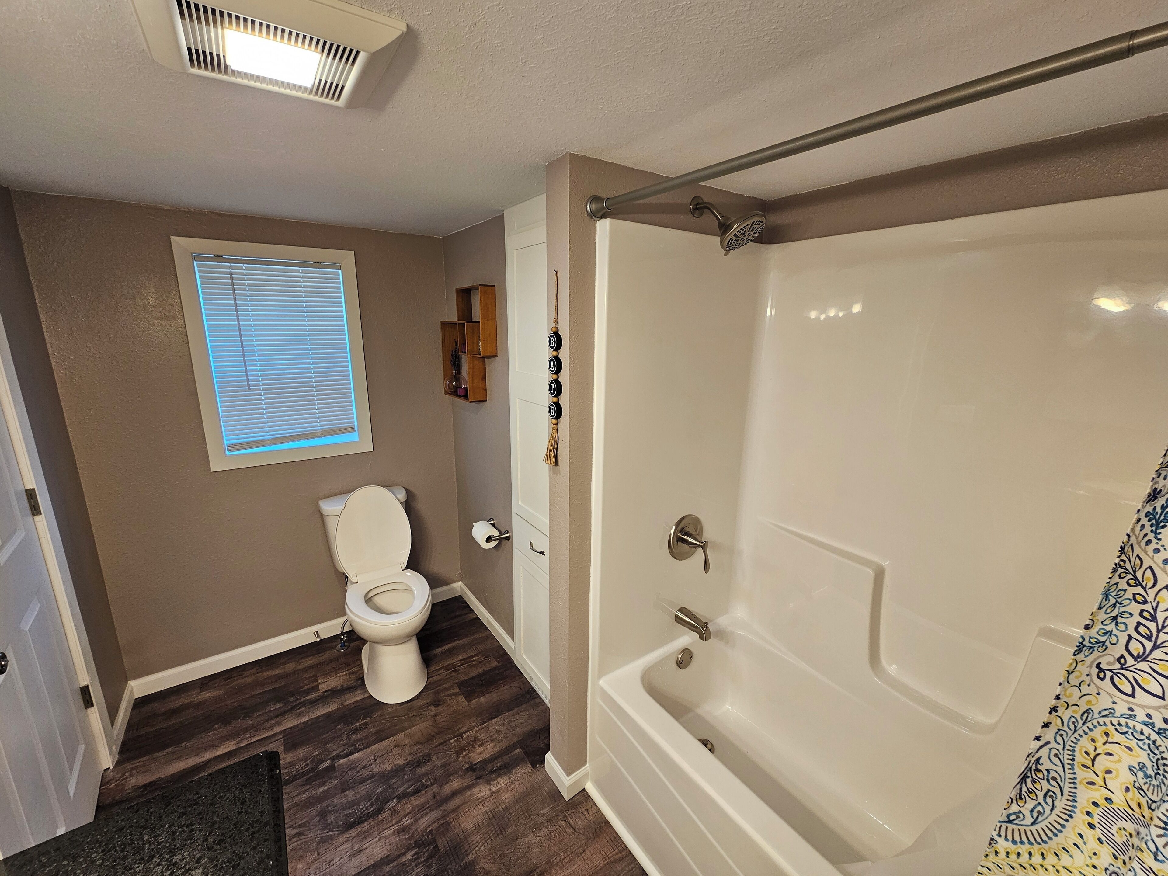 A bathroom with a toilet, a shower, and a window.