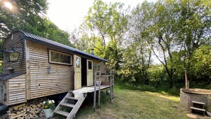 A wooden cabin with a porch, a ladder, and a stack of firewood.