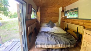 A cozy wooden cabin bedroom with a bed, a window, and a wooden ceiling.