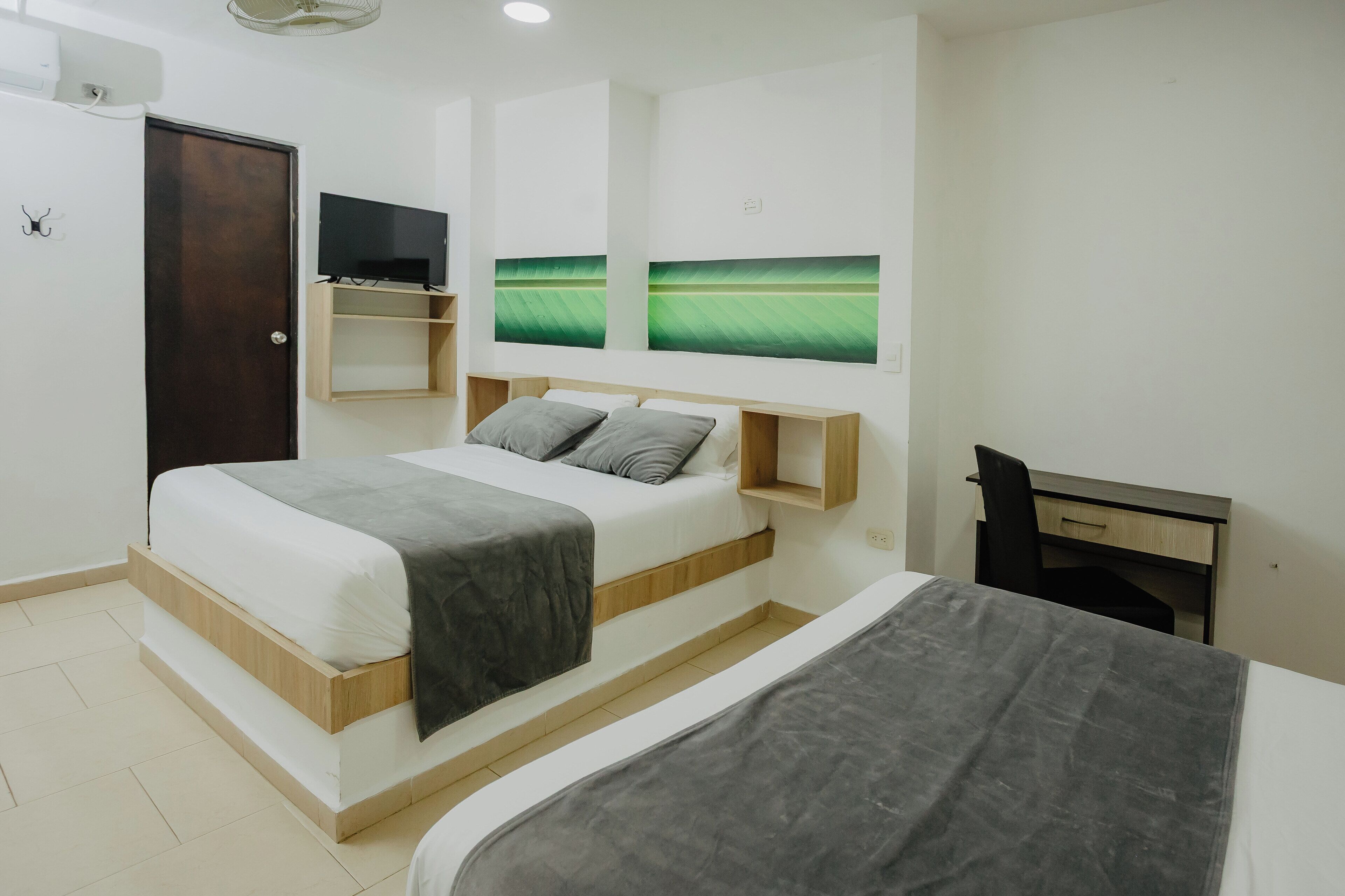 A modern bedroom with a bed, a desk, and two wall-mounted TVs.