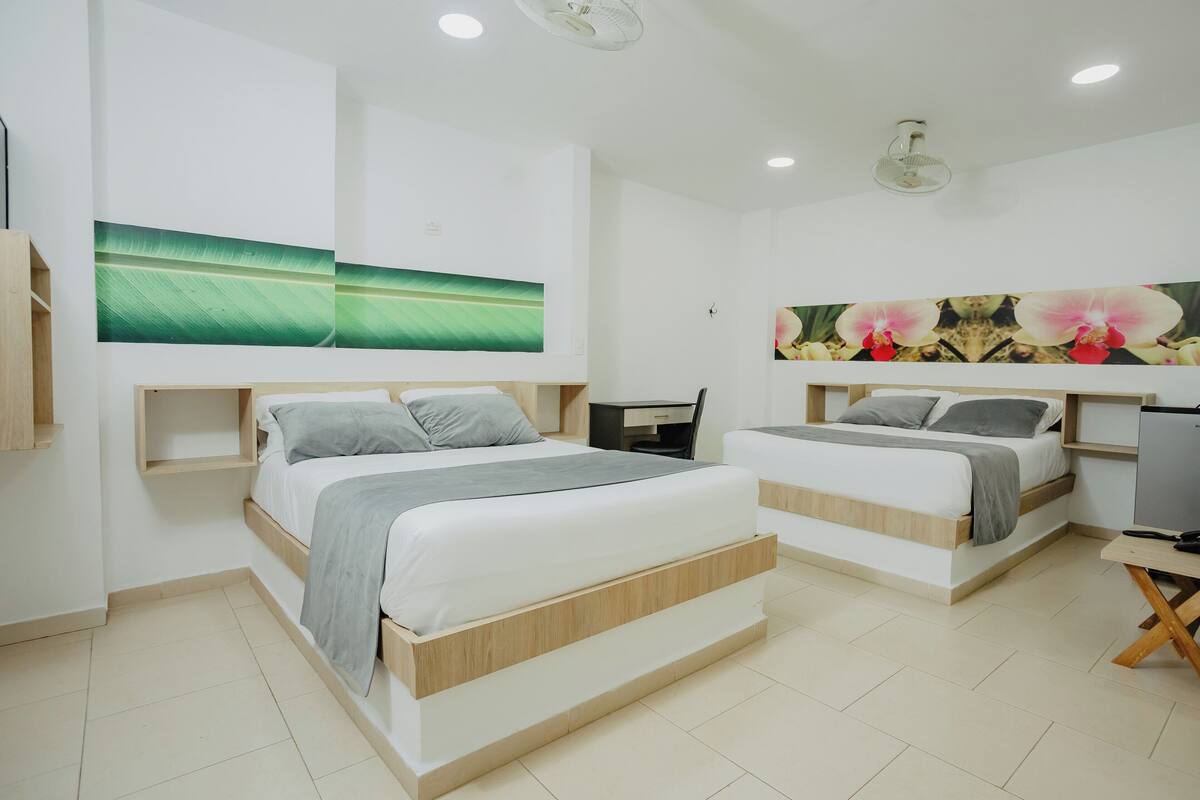 A modern bedroom with two beds, a desk, and a TV.