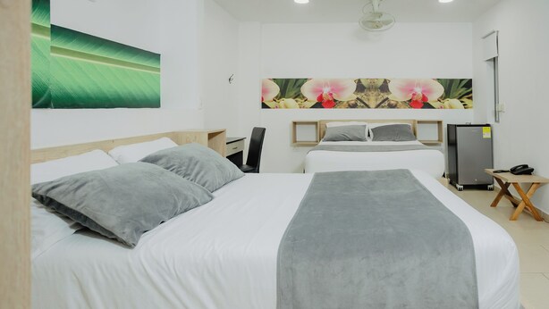 A hotel room with a bed, a desk, a chair, a refrigerator, and a wall-mounted phone. - Hotel Plataneras Plaza (Apartadó)