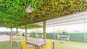An outdoor patio with tables and chairs, covered by a roof with green foliage. - Hotel Plataneras Plaza (Apartadó)