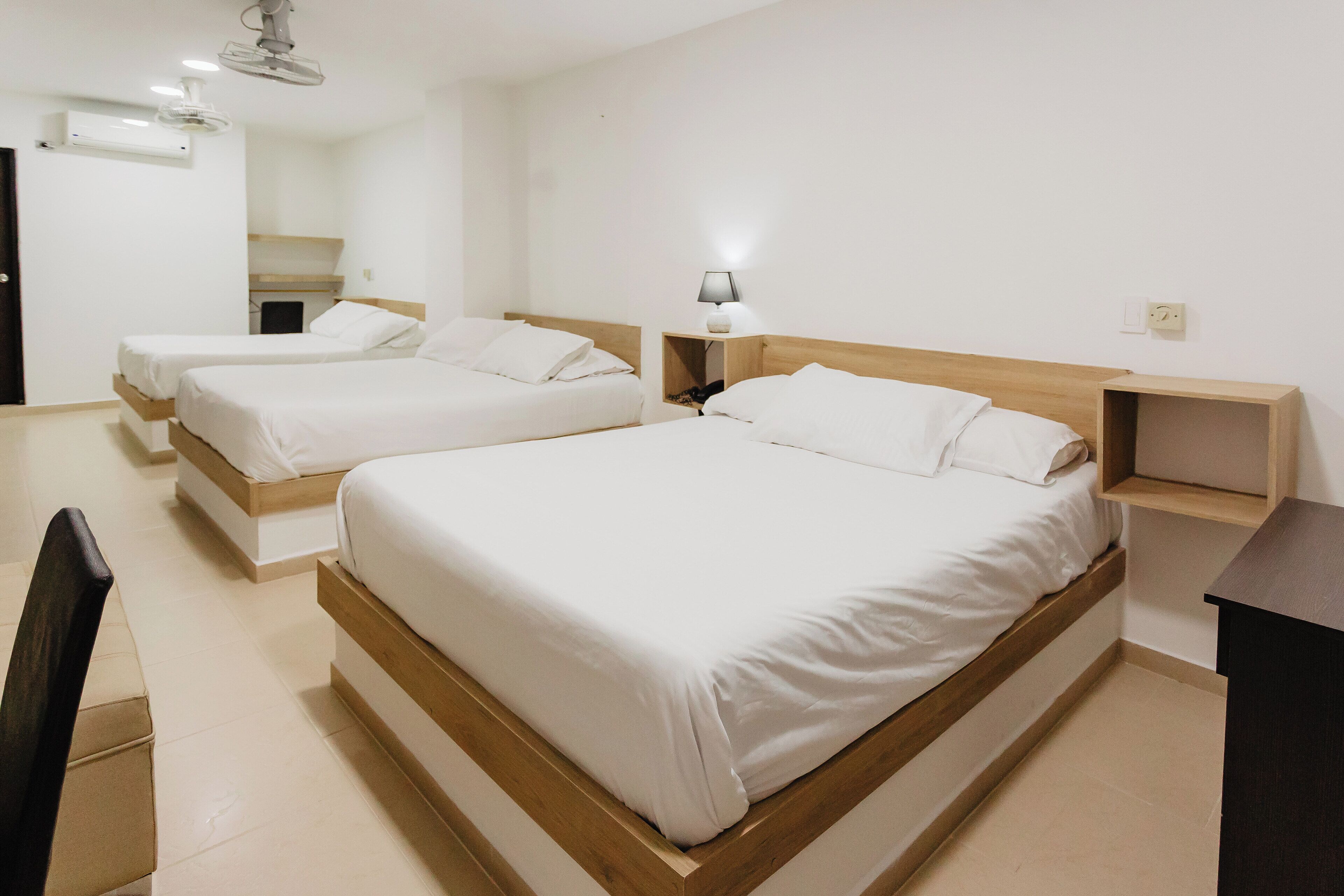 A hotel room with two single beds, a wooden headboard, a bedside table with a lamp, and a small shelf.