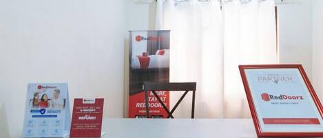 A hotel room with a bed, a table with promotional materials, a window with curtains, and an air conditioning unit.