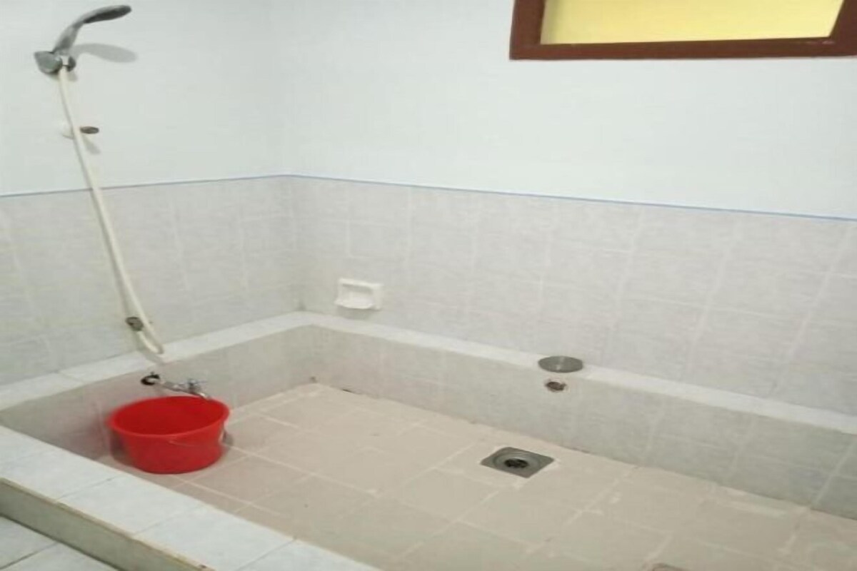 A bathroom with a bathtub, a red bucket, and a showerhead.