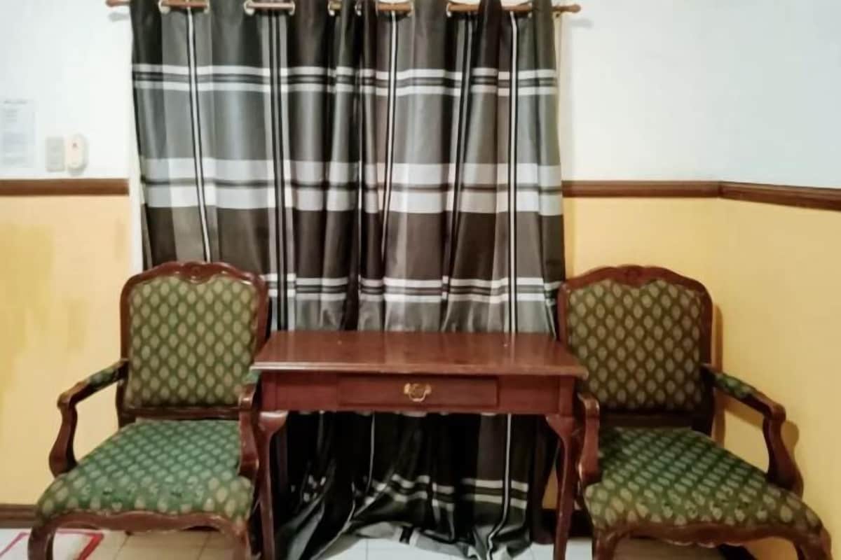 A room with two wooden chairs with green upholstery, a wooden table, and a striped curtain.