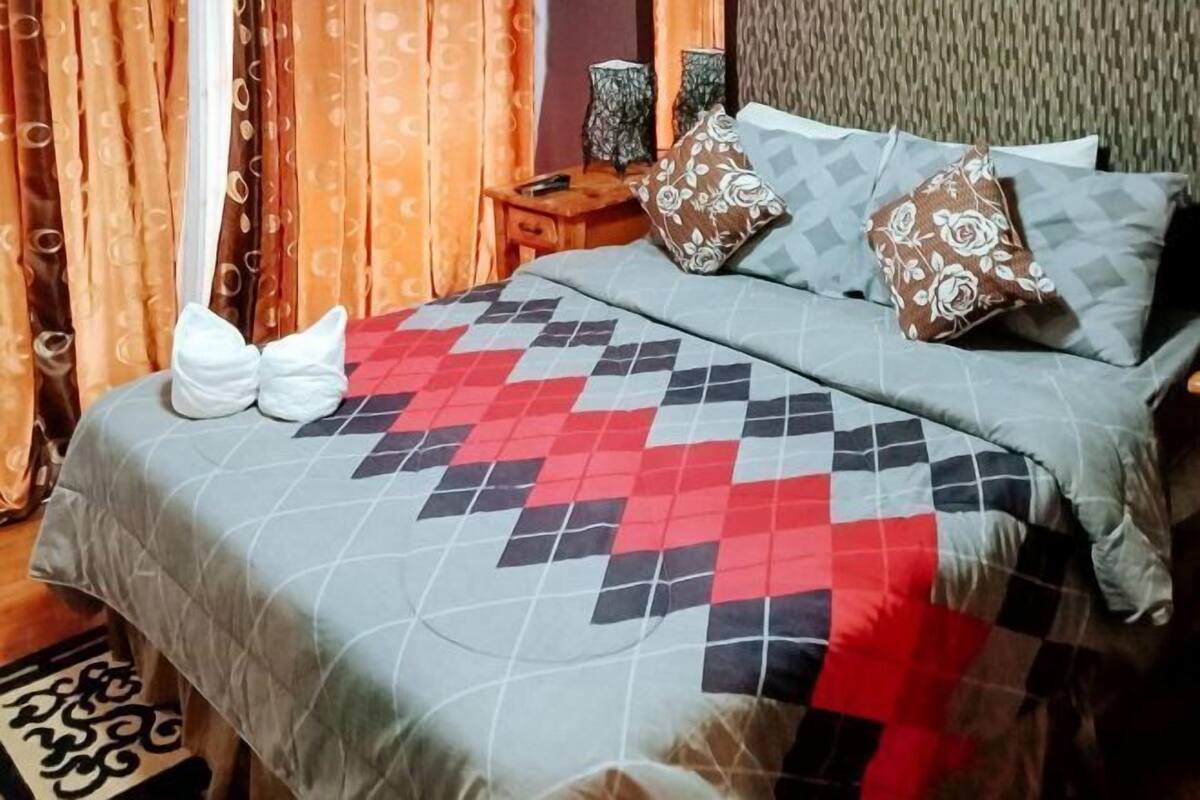 Ένα στρωμένο κρεβάτι με προσεγμένο τρόπο, με ένα διακοσμητικό κάλυμμα, ένα κομοδίνο με ένα φωτιστικό και κουρτίνες.