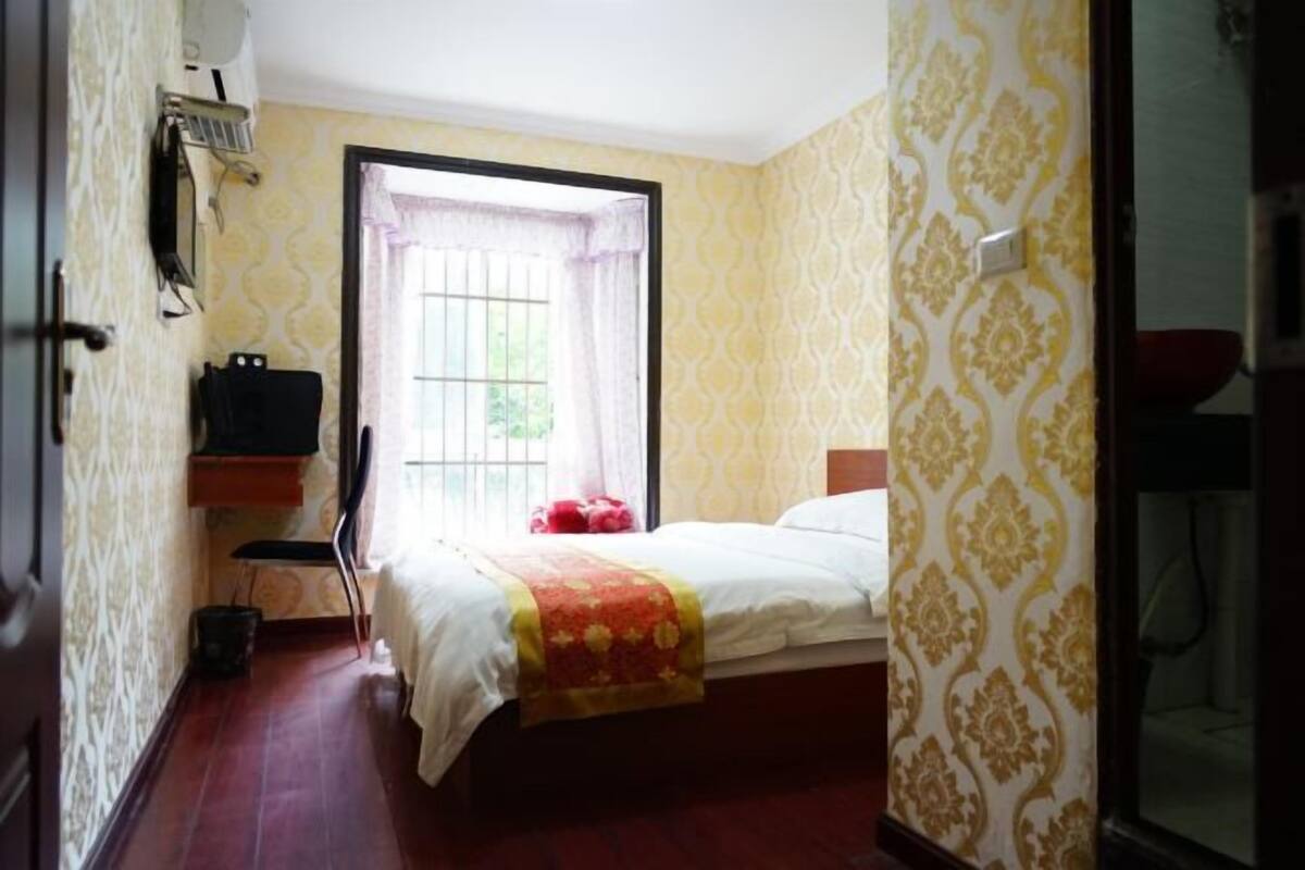 Ein Hotelzimmer mit Bett, einem Fenster mit Vorhängen, einem Nachttisch und einem Sessel.