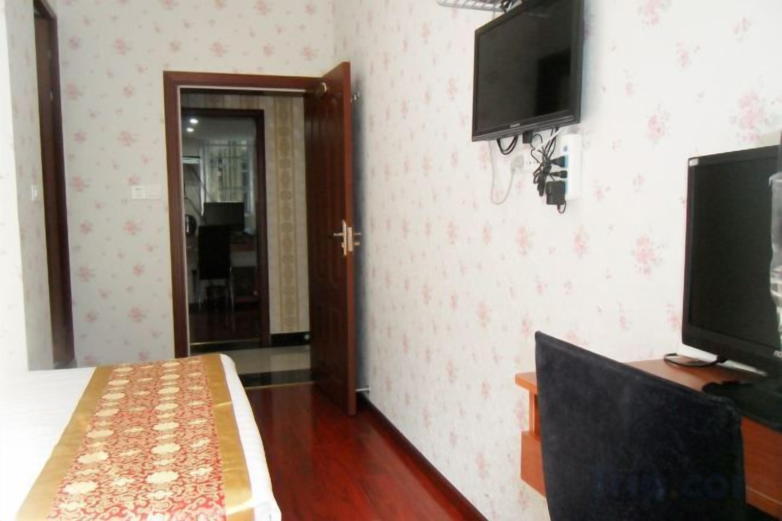 Quarto de hotel com uma cama, uma televisão e porta que dá para um corredor.