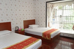 A hotel room with two beds, a window with a metal grill, and a patterned wallpaper.