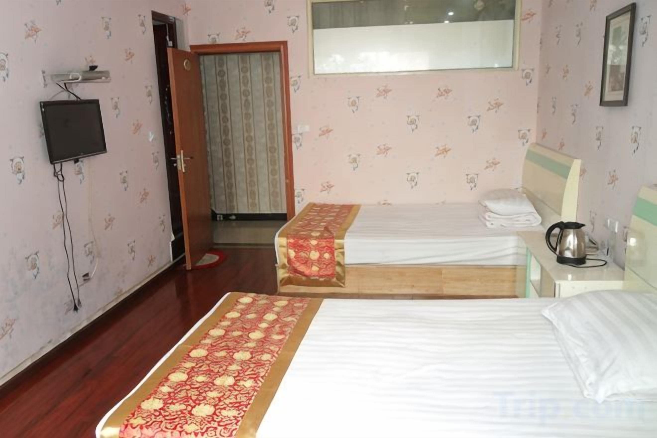 A hotel room with two beds, a television, a window, and a door leading to another room.