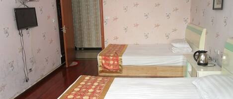 A hotel room with two beds, a television, a window, and a door leading to another room.