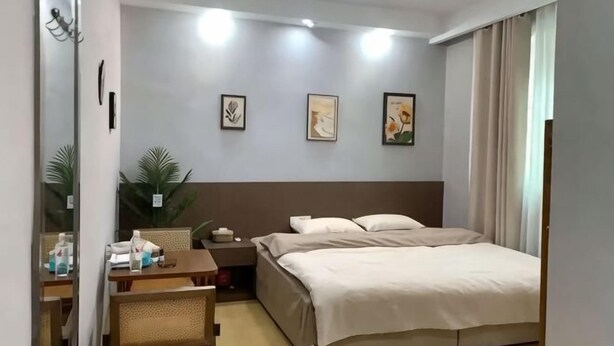A hotel room with a bed, bedside table, lamp, and wall art. - Wulong Youjia Hotel (Chongqing)