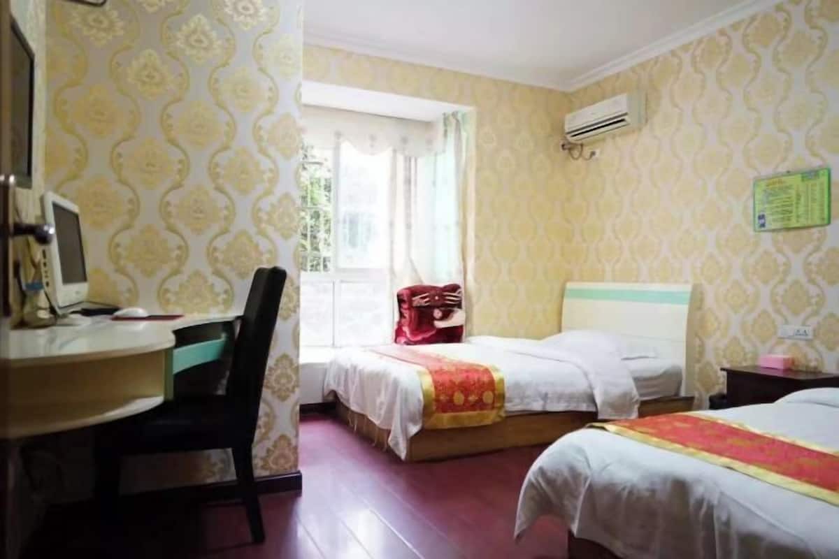 Ein Hotelzimmer mit zwei Betten, einem Schreibtisch mit Stuhl, einem Fenster mit Vorhängen und einer Klimaanlage.