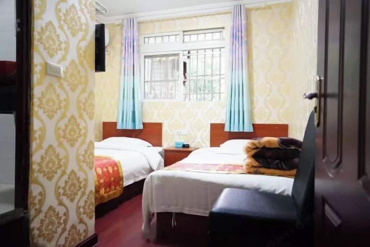 Ein Hotelzimmer mit zwei Betten, einem vergitterten Fenster, strukturierten Tapeten und einem Stuhl.