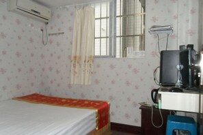A room with a bed, a desk with a computer, an air conditioner, and a window with curtains.