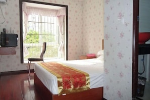 A bedroom with a bed, a chair, a window with curtains, a bedside table, and a wall-mounted TV. - Wulong Youjia Hotel (Chongqing)