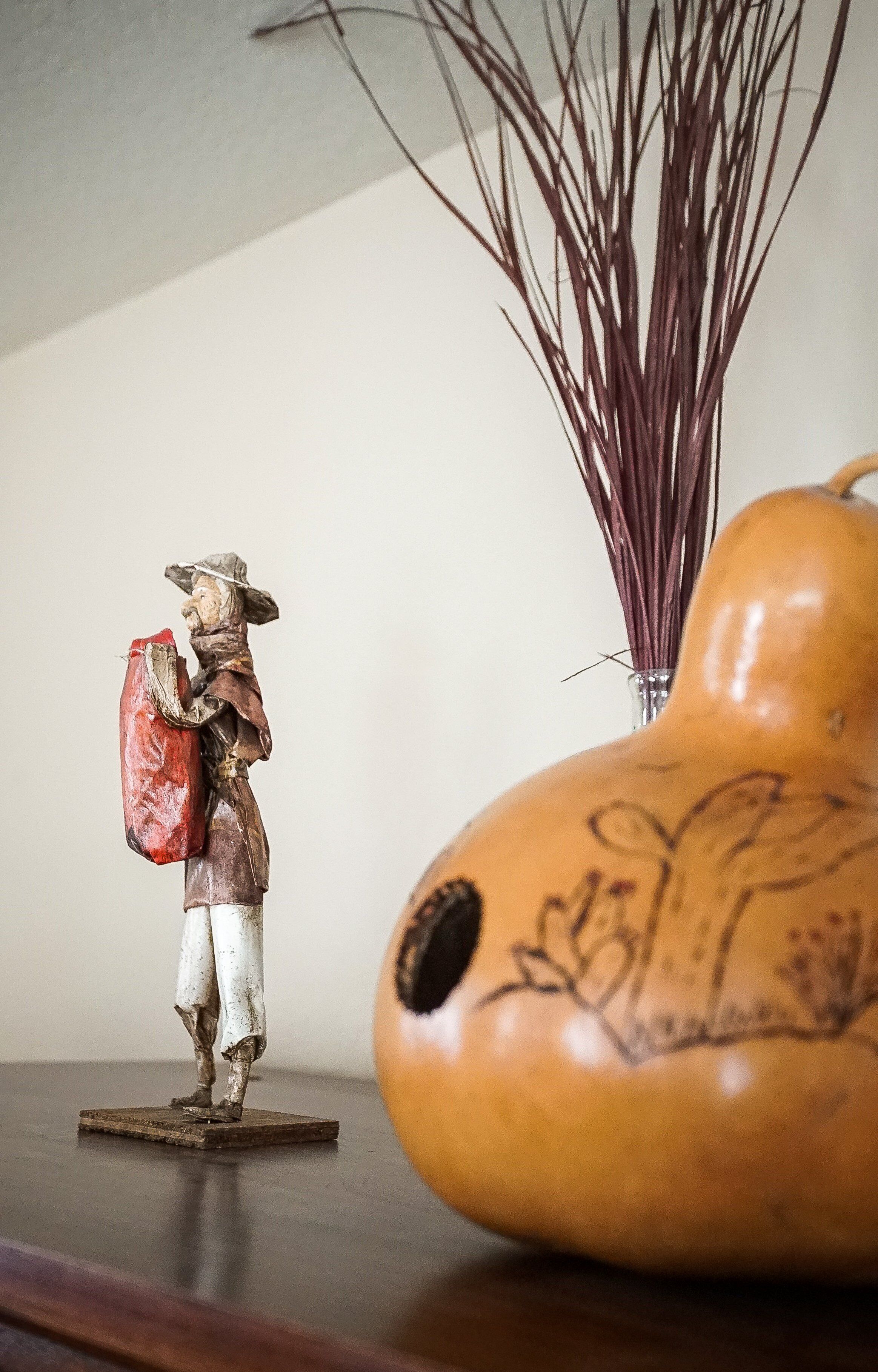 A wooden figurine of a person with a hat and a red bag on a table.