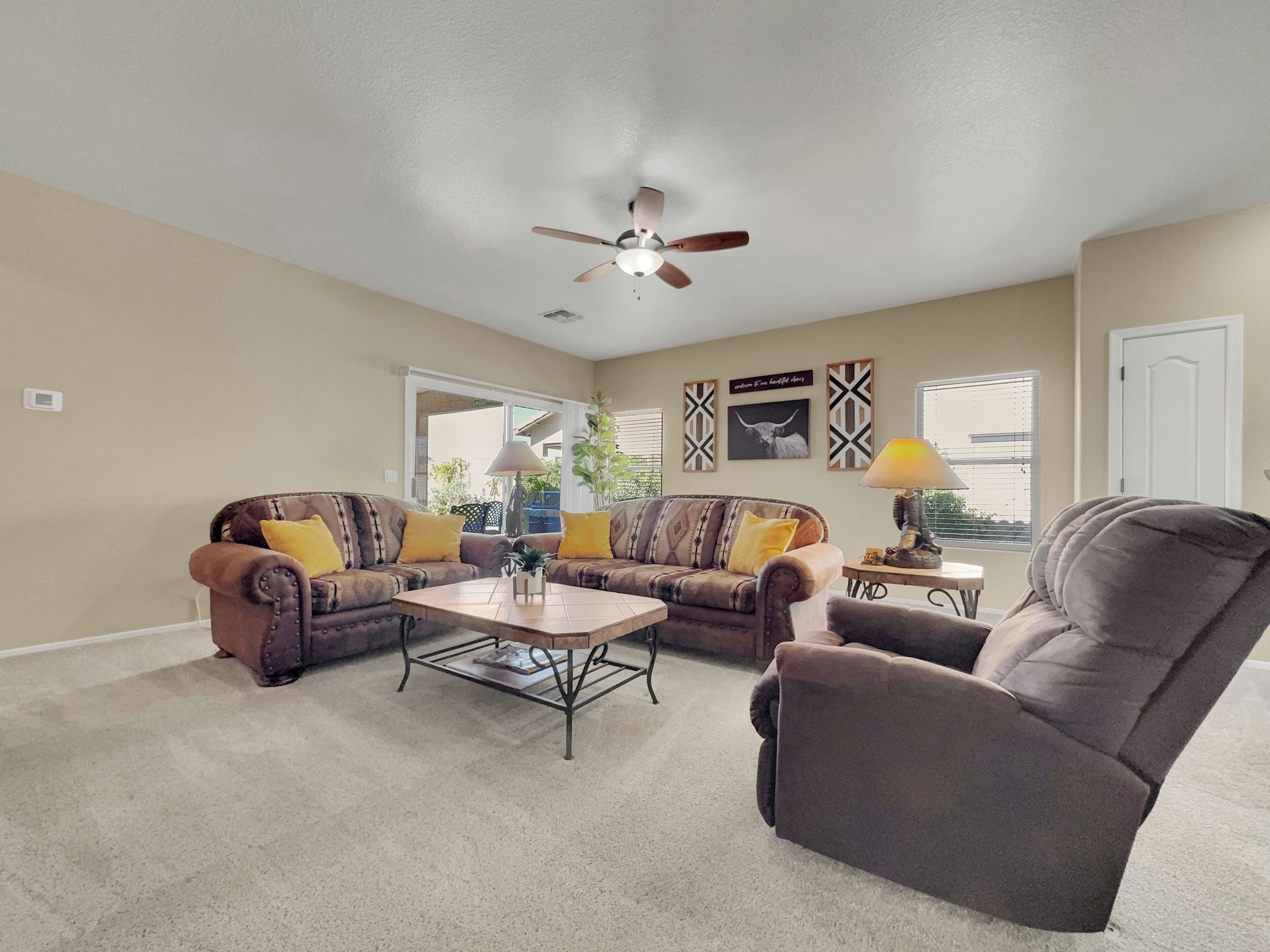 Ein Wohnzimmer mit Deckenventilator, zwei Sofas mit gelben Kissen, einem Couchtisch und einem Sessel.