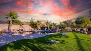 A backyard with a swimming pool, palm trees, and a patio area with chairs and a table. - Creekside Queen Creek (Queen Creek)