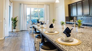 A modern kitchen with granite countertops, bar stools, pendant lighting, and a view to the outdoors. - Creekside Queen Creek (Queen Creek)