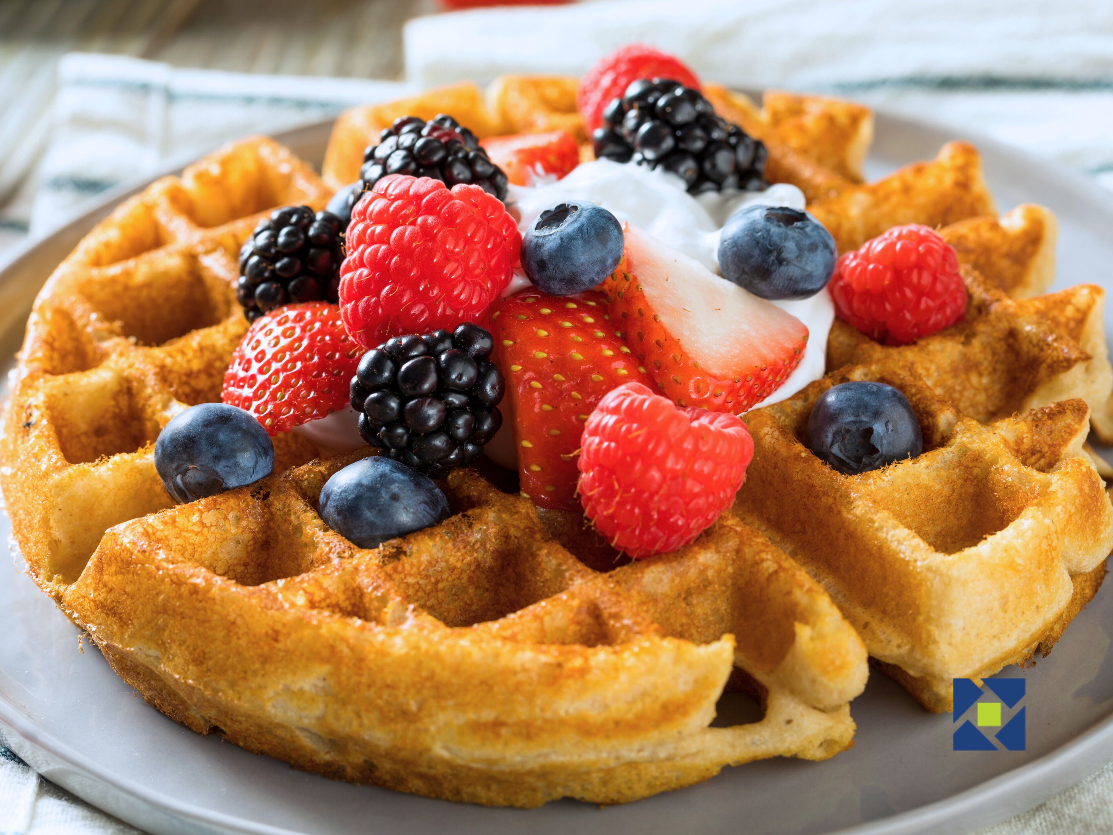 Un plato de gofres belgas cubiertos de frutos rojos frescos y crema batida.
